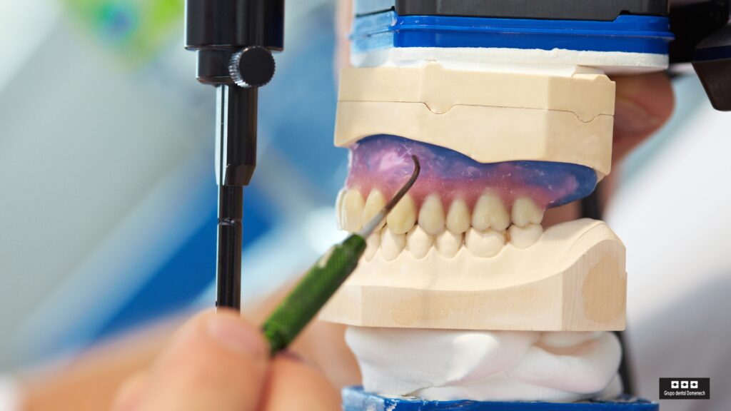 Modelo dental montado en un articulador que muestra el encaje entre los dientes superiores e inferiores, con un instrumento dental junto a la arcada superior.